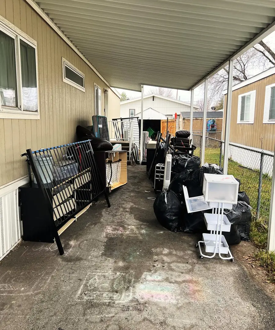 Carport packed with a bed frame, dresser, shelving and bags before the pickup